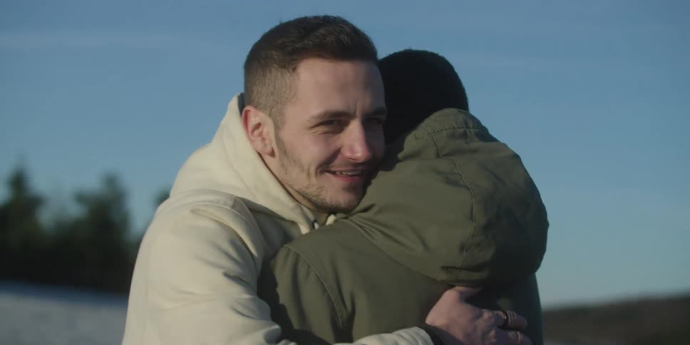 Man hugging another person outdoors during the daytime both wearing jackets