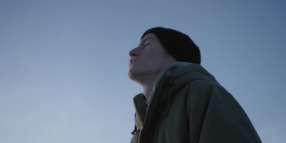 A distressed man gazes ahead in silence outdoors under a pale sky