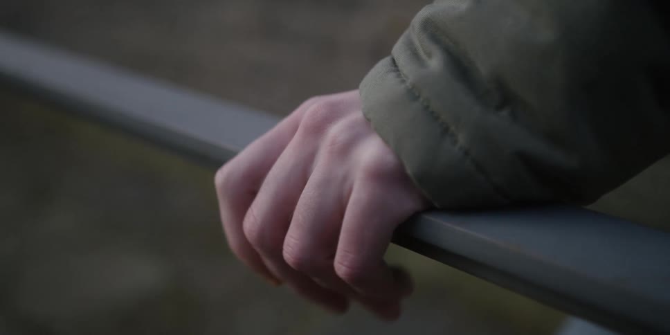 Hand resting on a metal railing with a green jacket sleeve visible