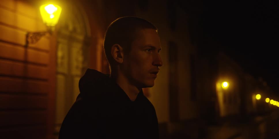 Man in profile on a street lit by lampposts at night