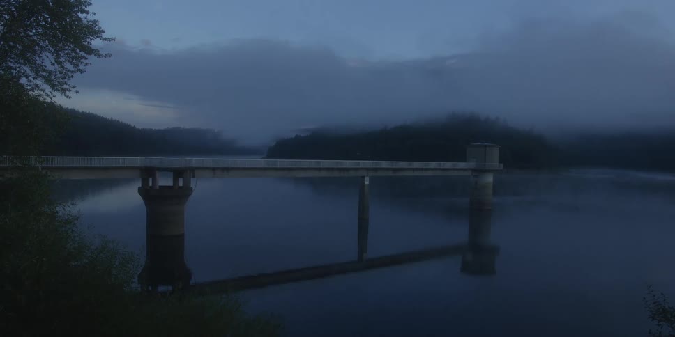 Bridge over a lake with pillars reflected in the water under a cloudy evening sky
