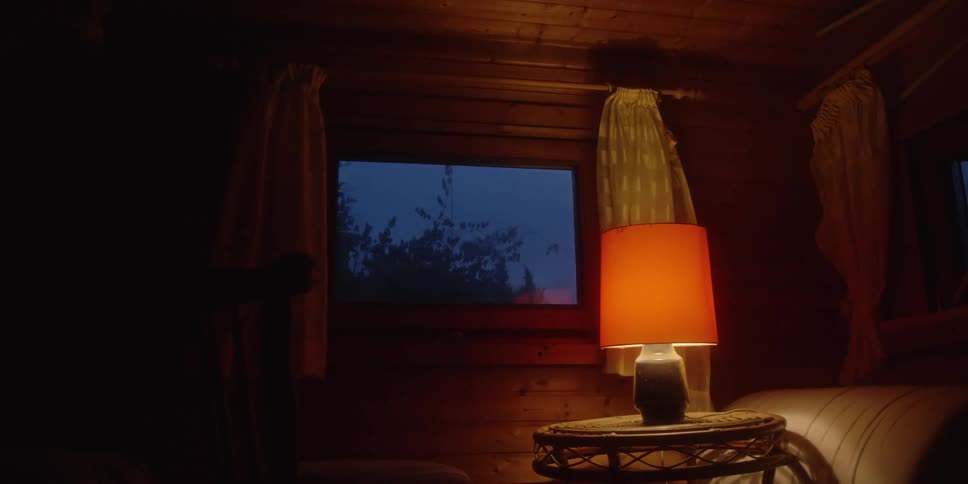 Lit table lamp beside a bed in a wooden room at night