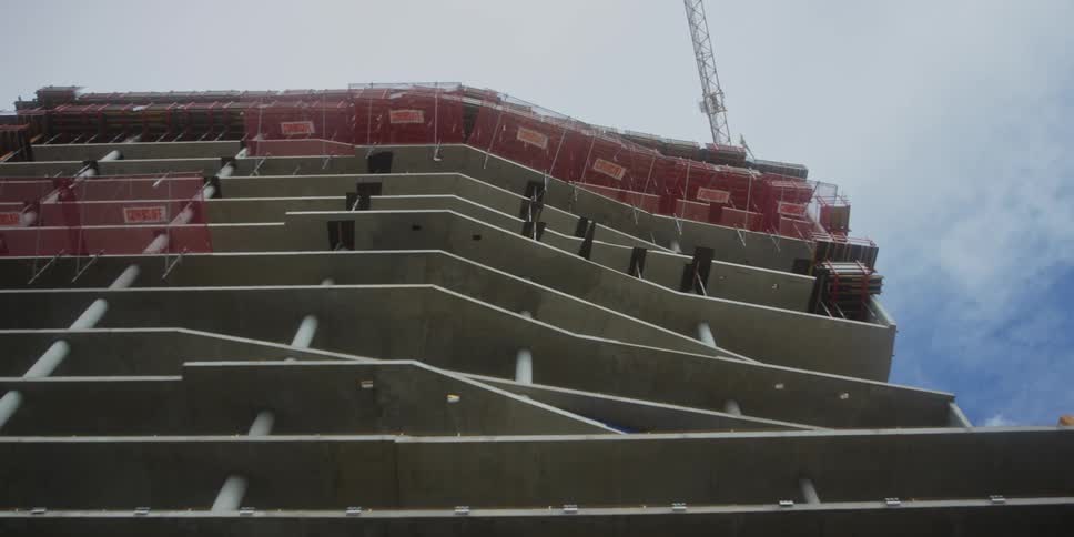 A construction site of a highrise building at midday with a crane towering above the structure