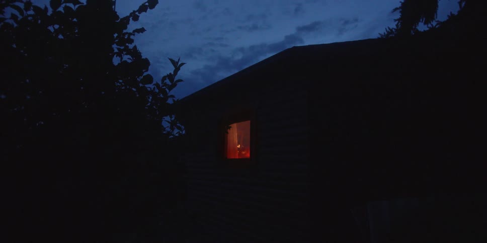 Dark house at night with a warmly lit window under a blue sky
