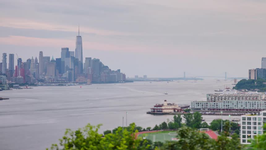 A cinematic timelapse captures the iconic new york city skyline across the hudson river where ferry boats dart across the gray water and clouds drift rapidly past the towering skyscrapers