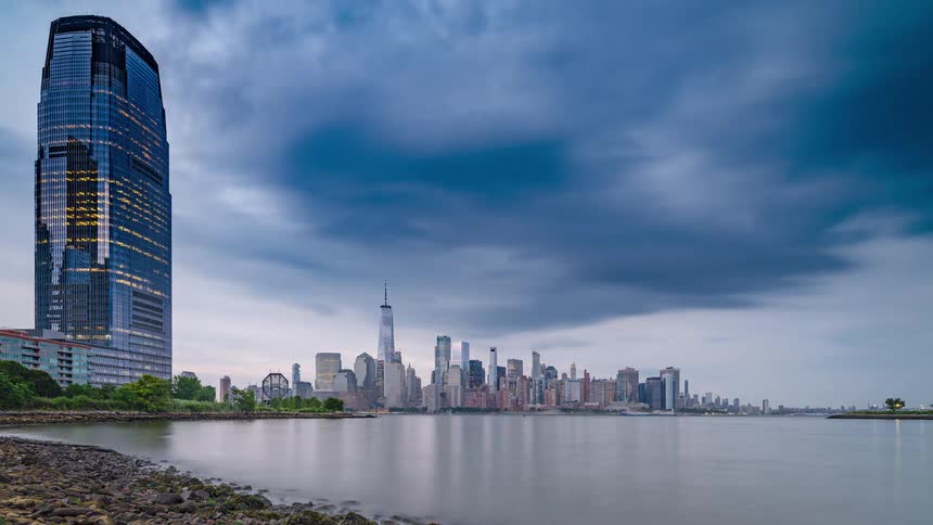 Boats sail on the water of a metropolitan coastal city with modern towers and buildings on the skyline as day turns to night