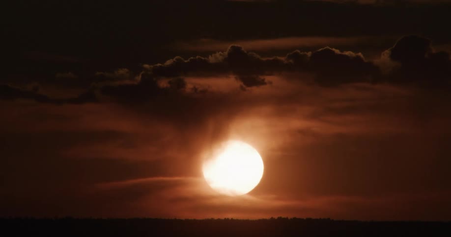 Haze covers the bright sun in a red sky on a cloudy day