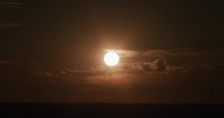 Low sun in the sky among layers of clouds above a dark horizon