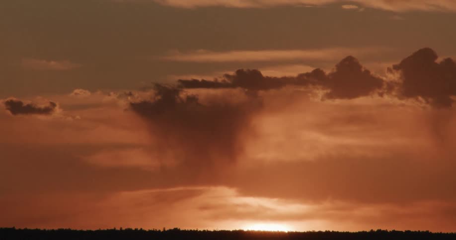 In a stunning timelapse the bright morning sun ascends behind dark shifting clouds casting a warm orange glow across the entire sky