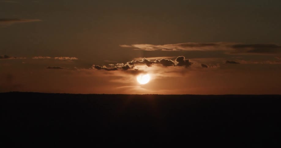 Moving over a rural area toward the sun glowing through clouds in a dark sky