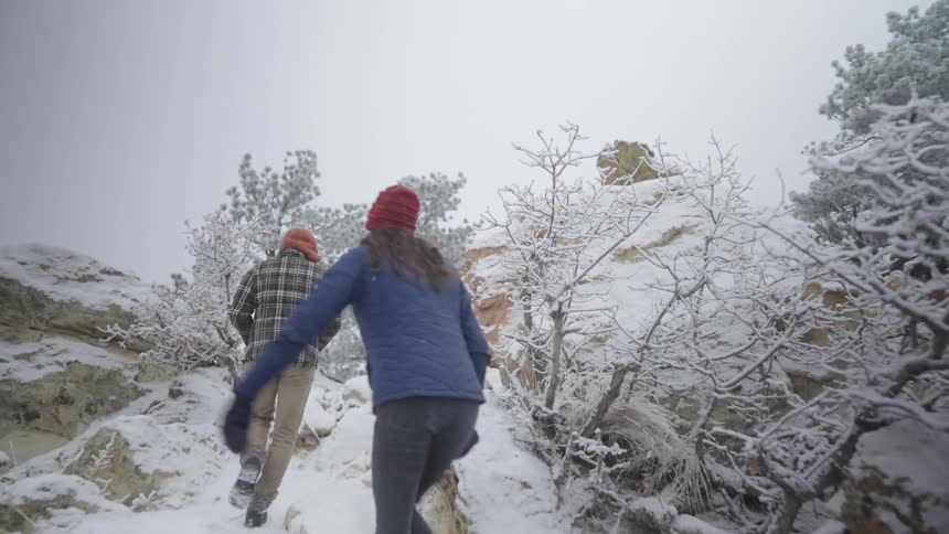Two young people walk up a snow covered mountain with ice covered trees