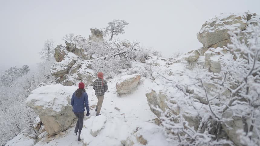 Two young people walk up a snow covered mountainside with ice covered trees