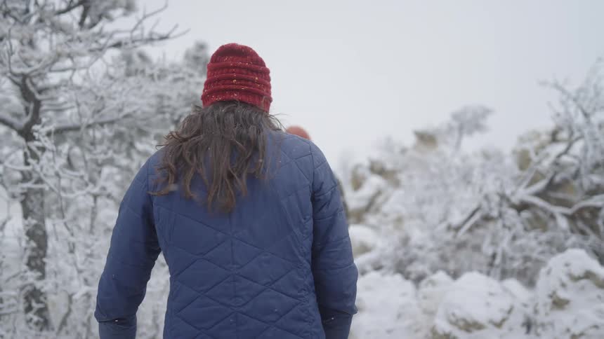 Two young people walk up a snow covered mountainside with ice covered trees