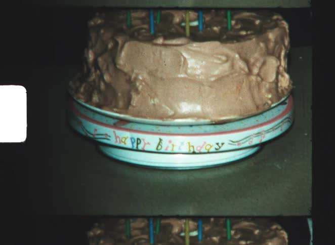A hand carefully adjusting a frosted birthday cake with candles on a table