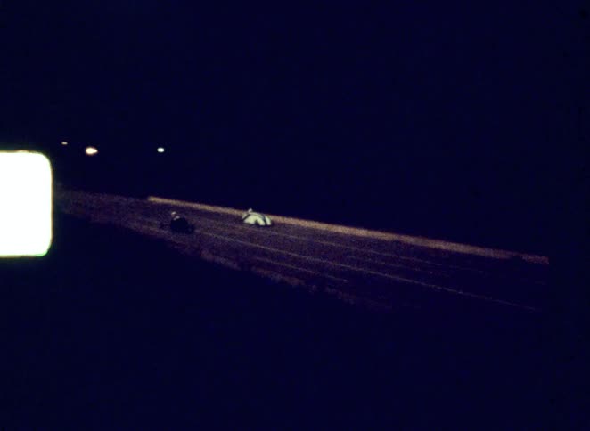 A racing track at night with two people speeding sidebyside in their race cars under the glow of track lights