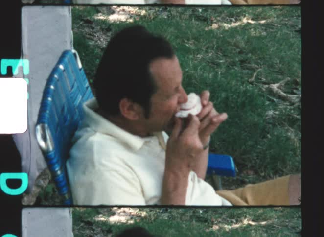A man eating a piece of fruit while sitting in a lawn chair outdoors