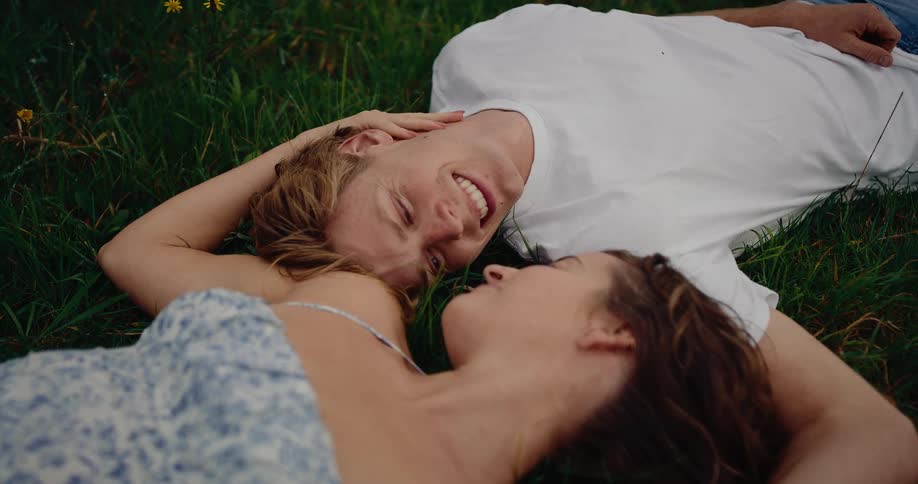 Couple lies on the grass in opposite directions and smiles into each others faces on a summer day