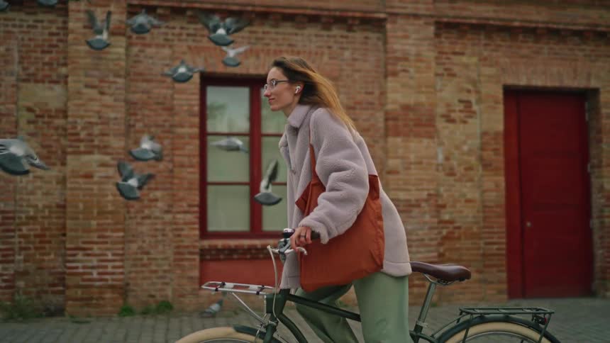 Woman riding a bicycle on a paved urban street beside a brick building