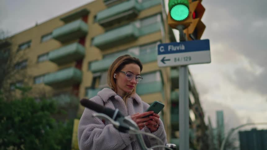 A woman checks her smartphone beneath a green traffic light at a busy city crossing
