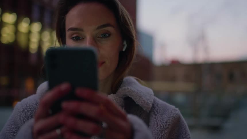 Woman stands outdoors on a winter day in the city and makes selections on her smartphone