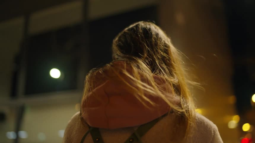Woman holds her smartphone while standing downtown and looking around at night