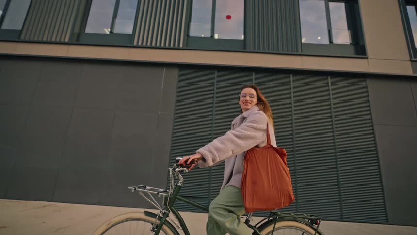 Woman rides a bicycle past an office building on a winter day