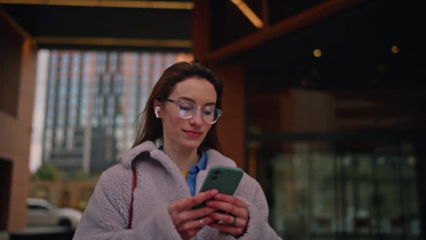 Smiling woman uses her smartphone while walking past a building downtown during the daytime