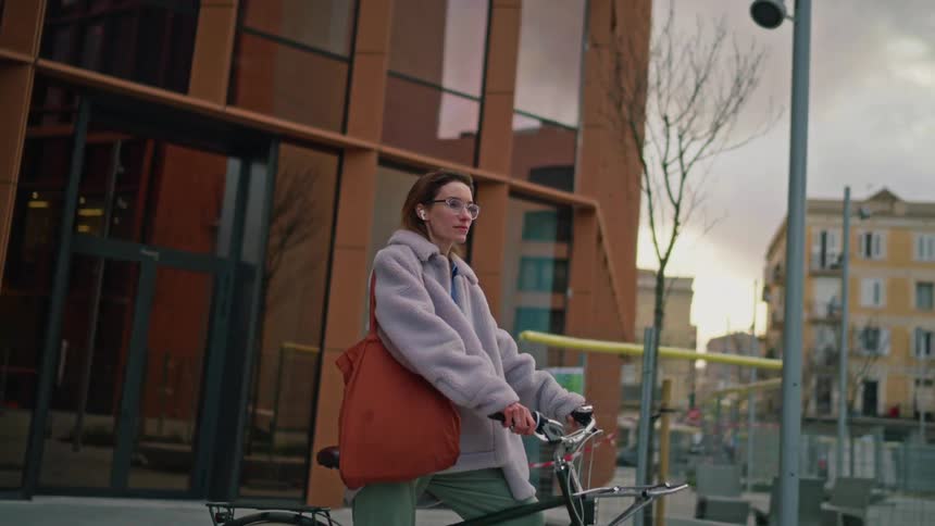 Woman riding a bicycle on an urban sidewalk in front of a modern glassfronted building