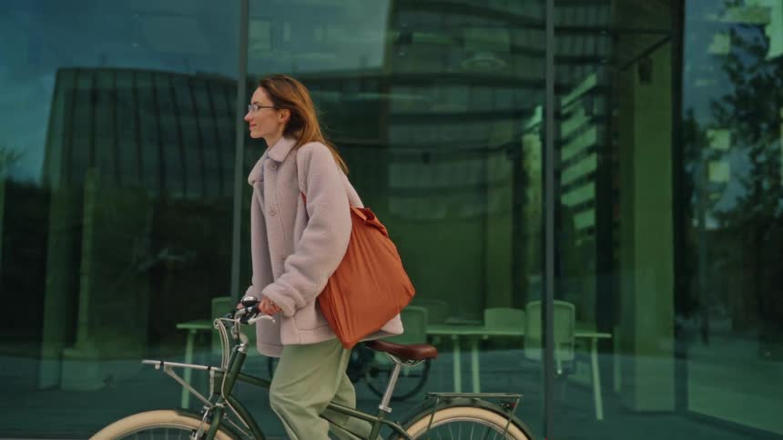 Woman riding a bicycle in an urban area beside a glassfronted building
