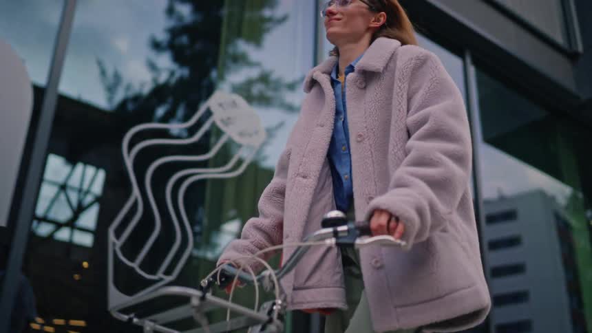 Woman rides a bicycle past an urban building with reflective windows on a winter day