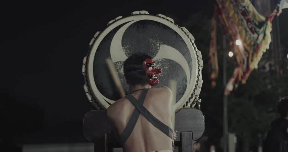 A man in a mask drumming outdoors at night