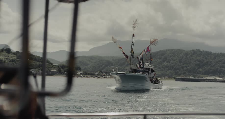 Decorated fishing boat with colorful flags sailing near mountainous coastline