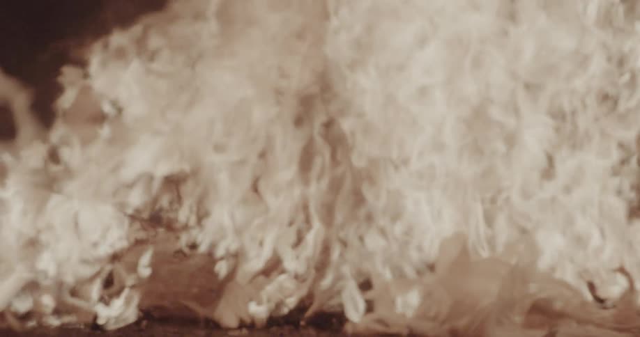 Large flickering flames consume a pile of debris casting a warm and intense glow across the scene the fire moves rapidly with dense smoke and shifting embers creating a sense of chaotic heat