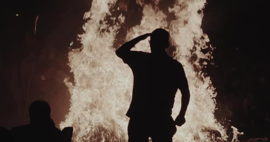 Man walks in front of a blazing bonfire