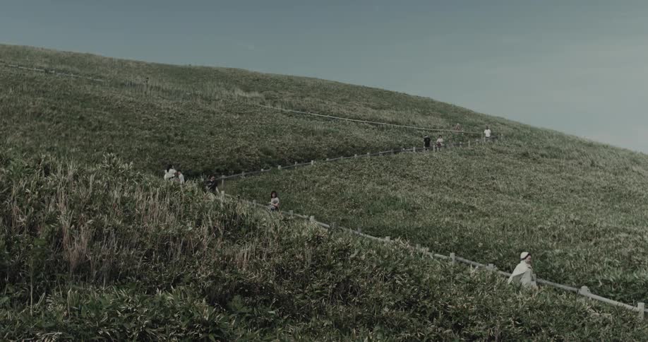 Hill grassland at midday with people walking along a path lined with a railing fence