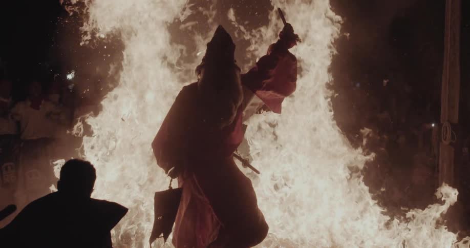 Person crossing intense flames during a ritual with onlookers nearby
