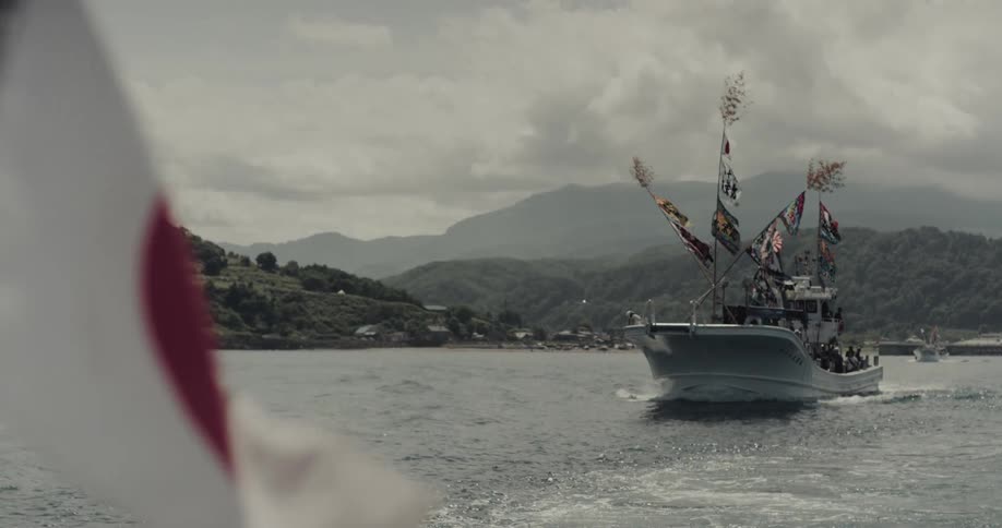 Decorated boat with colorful flags sailing near japanese coastal village under cloudy sky