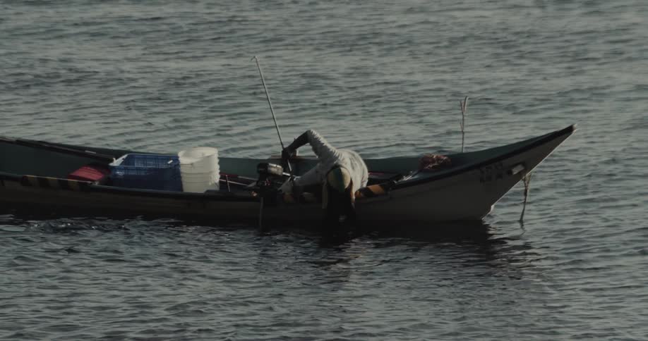 Man leans over in the boat while trying to access a trap during the daytime