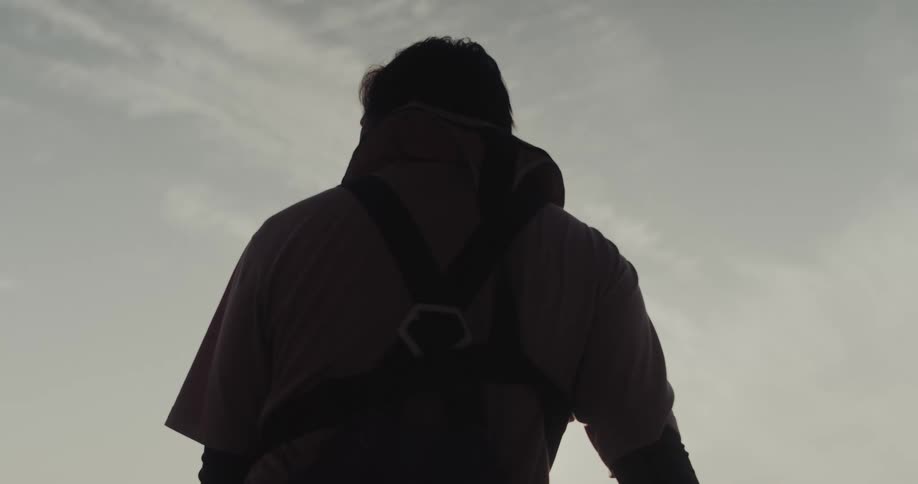 A person wearing a harness is silhouetted against a bright cloudy sky