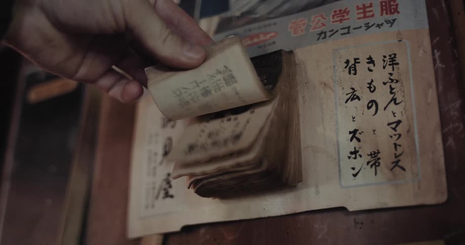 Hand flipping through an old calendar with japanese characters attached to a wall