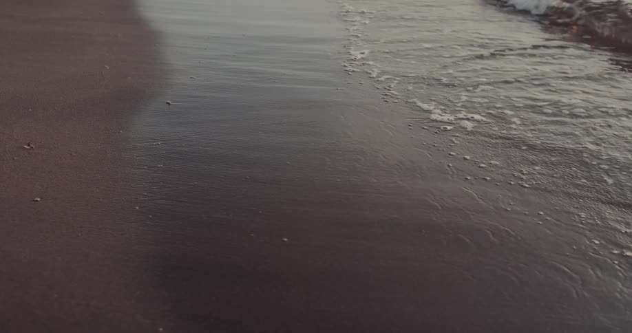 Gentle ocean waves reaching wet sandy shoreline