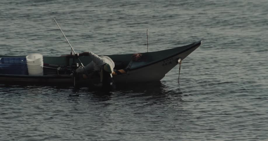 A person is tending to the motor of a small boat floating on choppy water