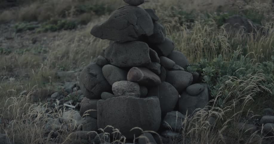 Stacked stones on dry ground with vegetation in the background