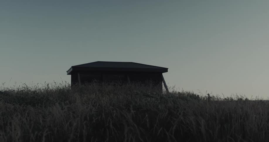 A small dark structure sits atop a grassy hill silhouetted against a pale overcast sky