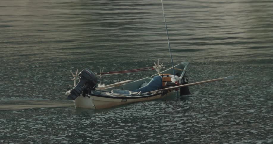 Fishing boat drifting alone on calm ocean water at midday with no one on board