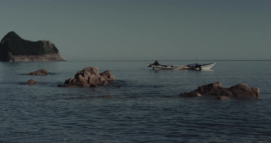 Fishing boat with two crew members floating on calm waters near forested island