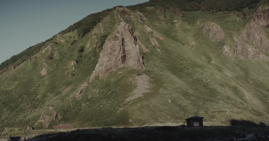 Sunlight shines on a mountain slope with a small building at the foot of the mountain