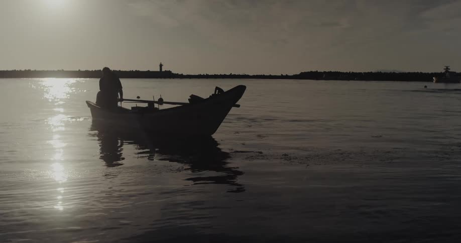 A man riding his canoe paddling away from the shoreline as the sun sets and warm light reflects across the water