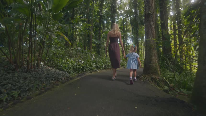 Adult and child walking hand in hand along a path in a forested area