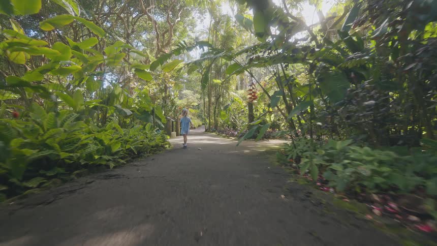 A child walking along a rainforest path at midday wearing a blue gown and blue sneakers as she moves through the lush greenery